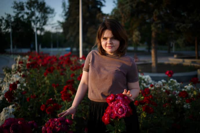 Zhenia poses with a rose bush at sunset in the centre of Kramatorsk, near the Palace of Culture and Technology