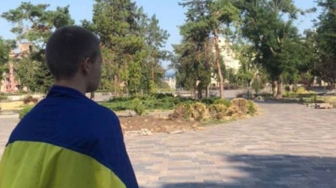 In occupied Mariupol, a young man leaves the Drama Theatre wearing the flag of Ukraine