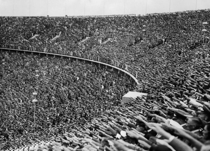 Натовп глядачів на Олімпійських іграх 1936 року в Берліні піднімає руки в нацистському вітанні на честь прибуття фюрера на стадіон